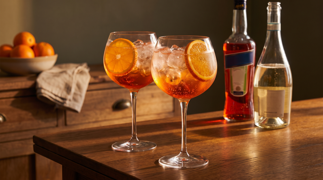 Two Aperol Spritz cocktails with orange slices on a dark-wood table in warm afternoon light