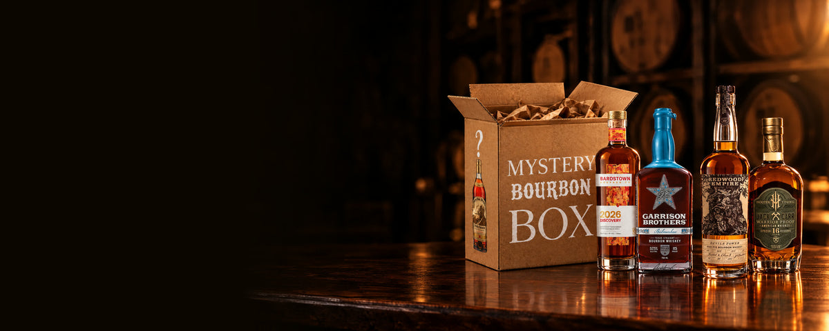 The Bourbon Mystery Box open on a walnut bar beside four small-batch bourbons