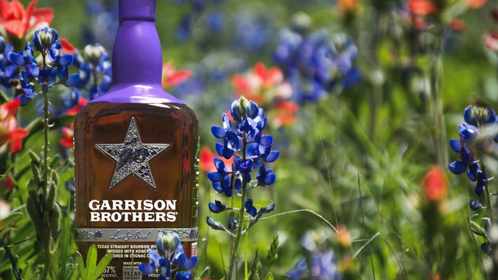 Garrison Brothers Lady Bird bottle in a field of Texas bluebonnets and Indian paintbrush